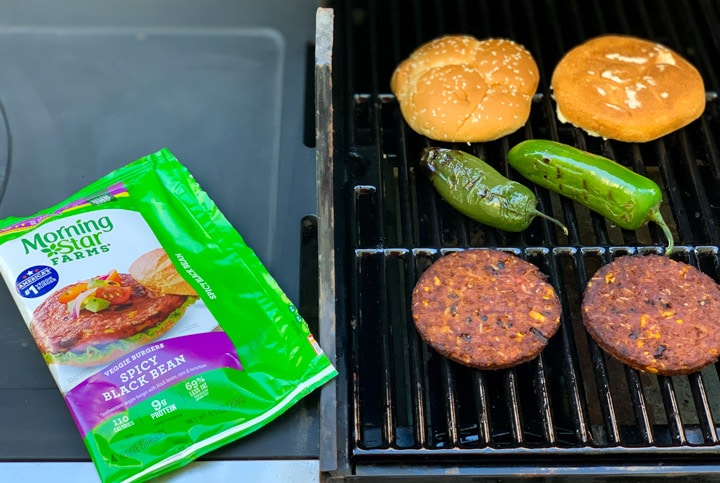 Morning star black bean burgers on a grill along with a bun and jalapeños