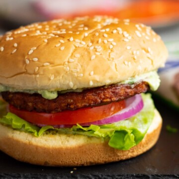 Burger with lettuce, tomato, onion and dressing flowing.