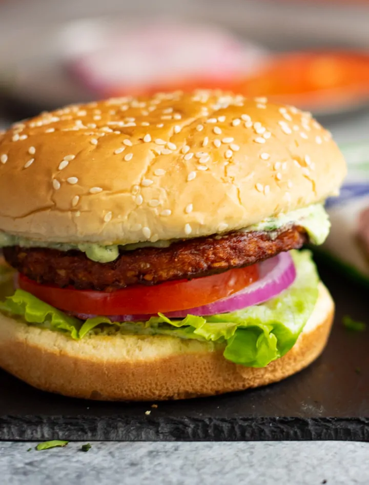Burger with lettuce, tomato, onion and dressing flowing. 