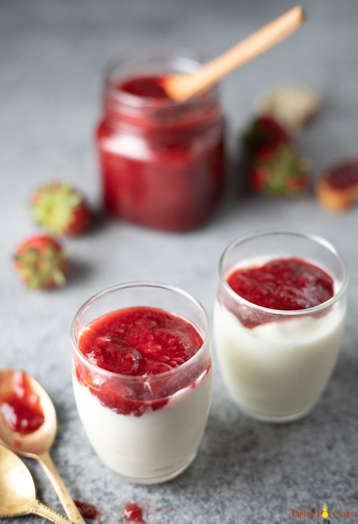 Yogurt topped with strawberry jam in 2 glasses and a jar of jam in the back