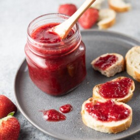 Strawberry Jam in a glass jar on a plate, along with jam spread on sliced bread