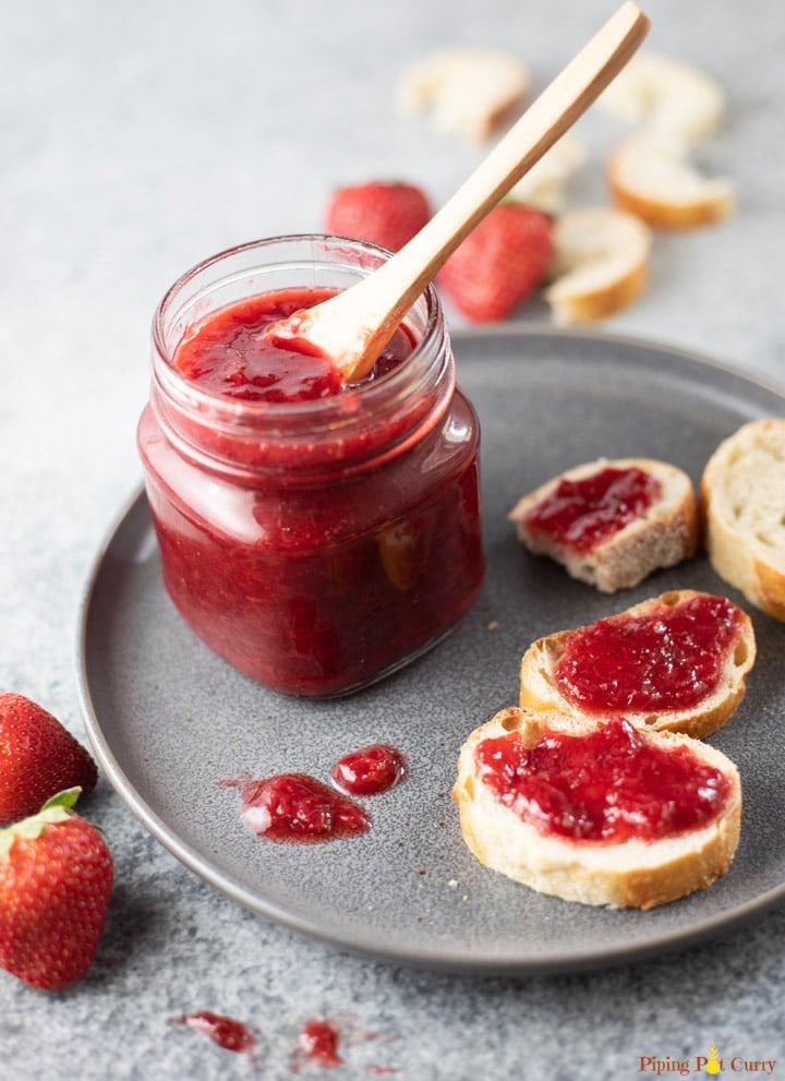 Strawberry Jam in a glass jar on a plate, along with jam spread on sliced bread