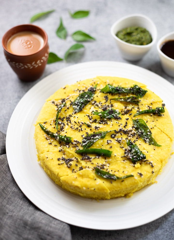 Khaman Dhokla garnished with tempering of curry leaves, along with chai and chutney.