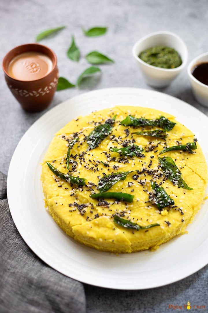 Khaman Dhokla garnished with tempering of curry leaves, along with chai and chutney.