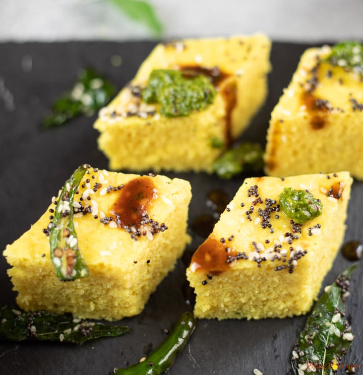 Four pieces of yellow Khaman dhokla on a black platter