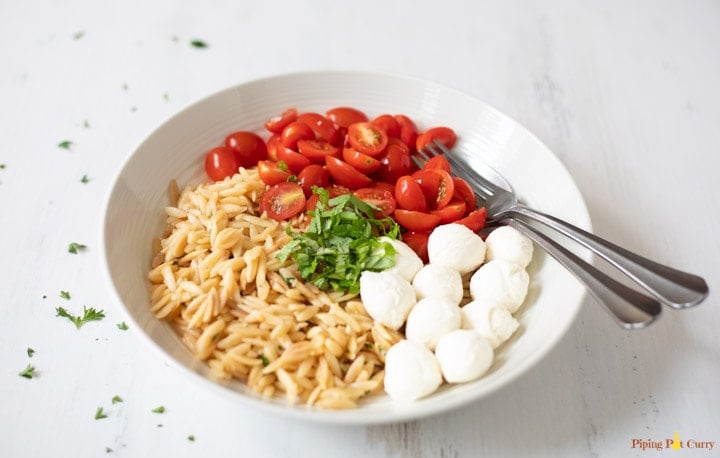 Orzo pasta, mozarella balls, cherry tomatoes and basil in a white bowl