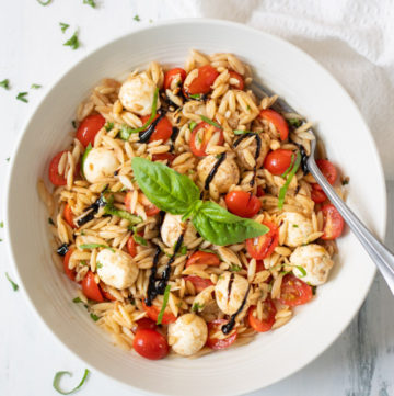 Caprese Orzo Pasta Salad in a white bowl garnished with balsamic and basil