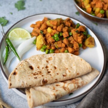 Aloo Gajar Matar (Potato, Carrots & Peas) along with roti (indian flatbread) in a white plate along with yogurt raita on the side.