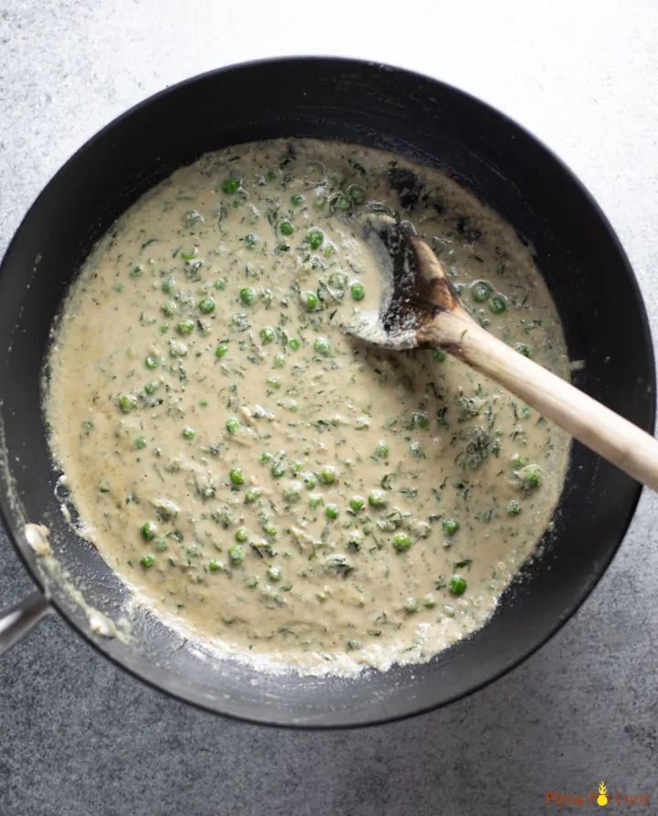 A curry with green peas in a white sauce in a wok