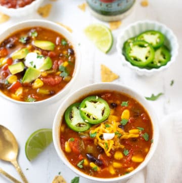 Two bowls of taco soup along with toppings spread out