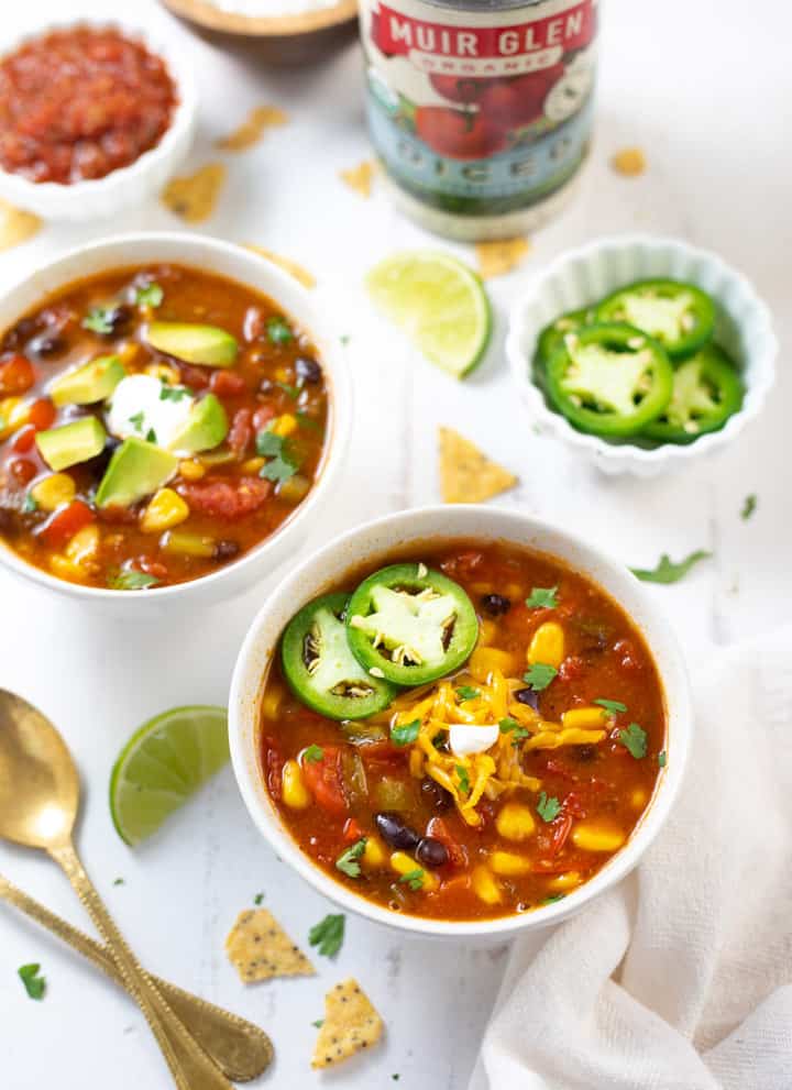 Two bowls of taco soup along with toppings spread out