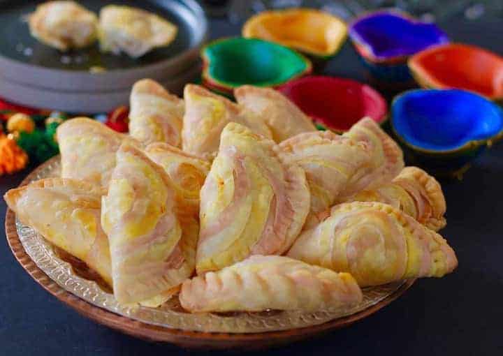 Rose Coconut Karanji in a plate with decorative divas in the back