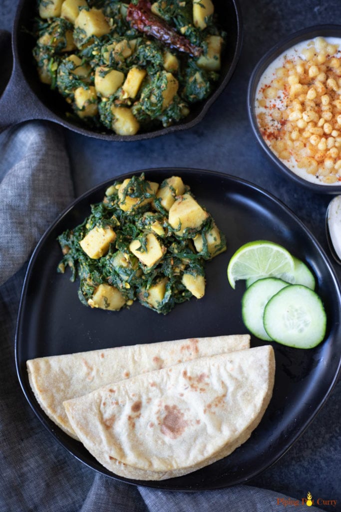 Aloo Palak served with chapatti on a black plate with lime and cucumber 