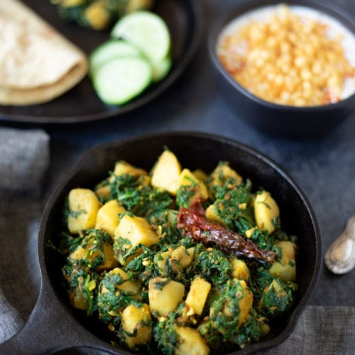 Aloo Palak (Potatoes & Spinach Stir Fry) in a cast iron skillet with raita and roti