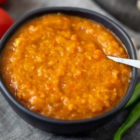 Indian curry sauce made with onions and tomatoes in a black bowl with spices and tomatoes in the back