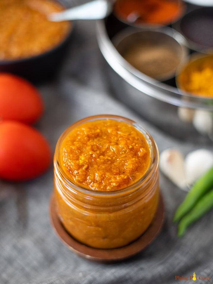 Indian curry sauce made with onions and tomatoes in a glass jar with spices and tomatoes in the back