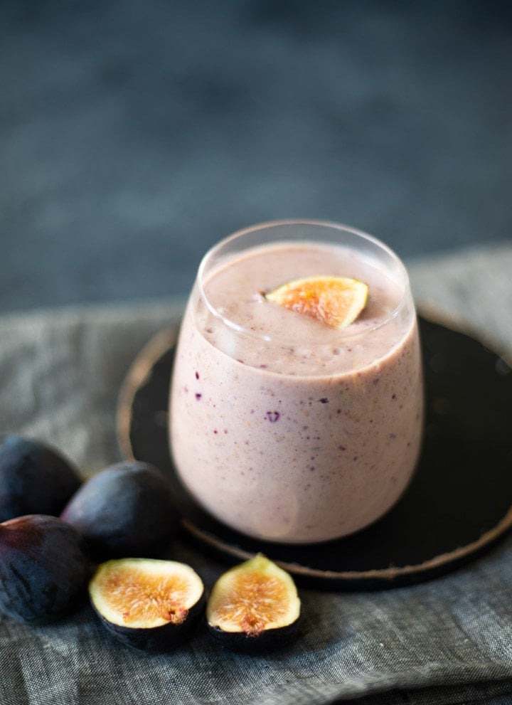 Fig smoothie with some figs lying beside the glass