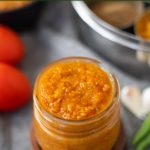 Indian curry sauce made with onions and tomatoes in a glass jar with spices and tomatoes in the back