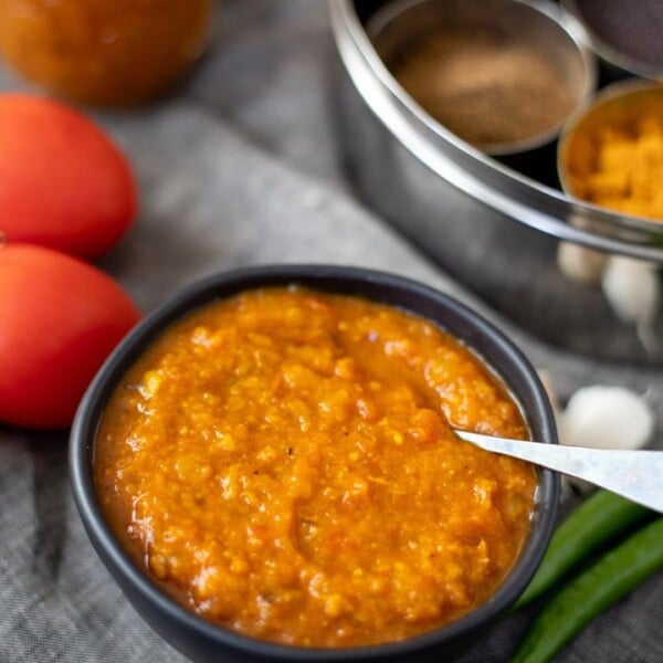 Indian curry sauce made with onions and tomatoes in a black bowl with spices and tomatoes in the back
