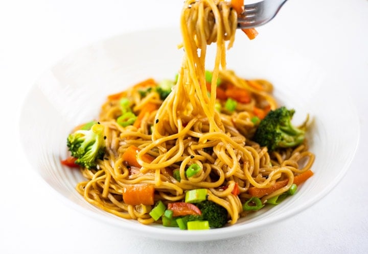 Lo Mein noodles with vegetables in a white bowl and being picked by fork