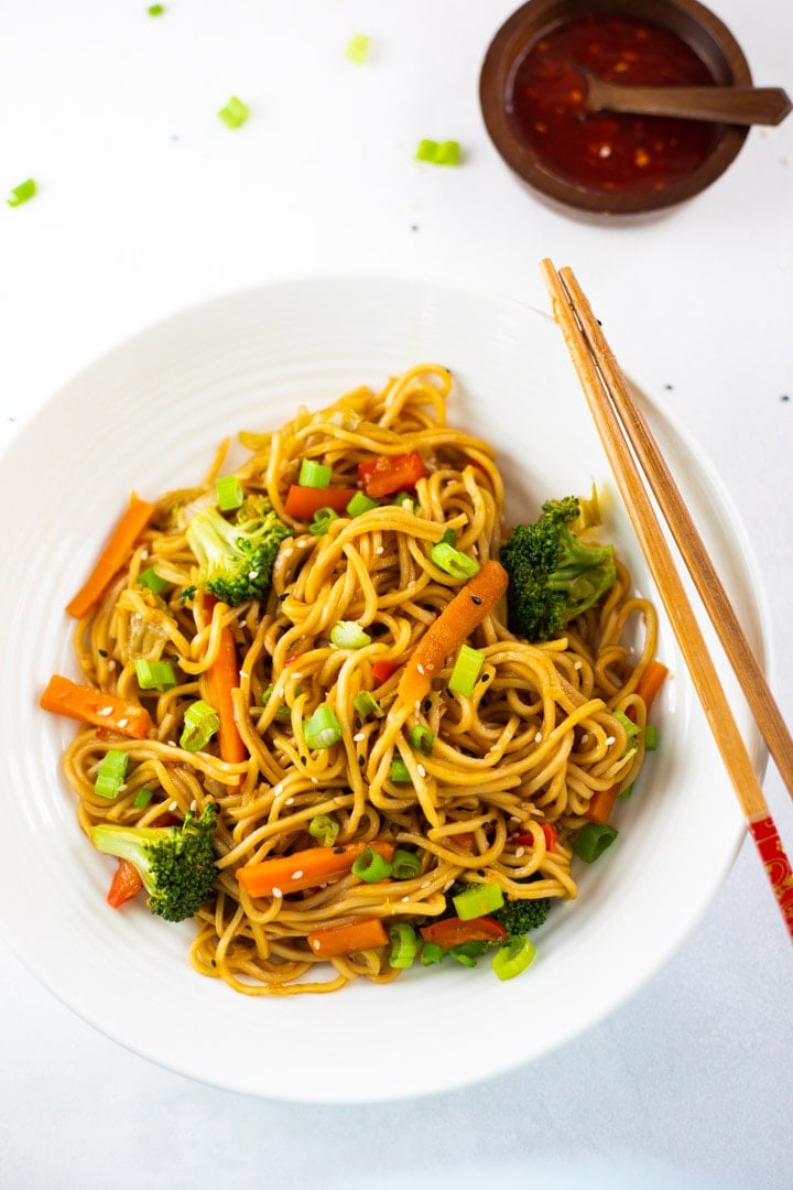 vegetable lo mein on a white plate with chopsticks and a side dish of sauce