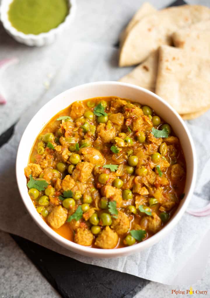 Soya nuggets and green peas curry in a white bowl with rotis in the side