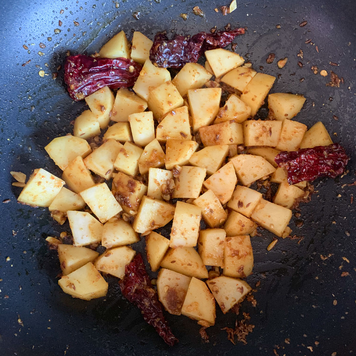 Cooked potato in a pan with dried red chili peppers. 