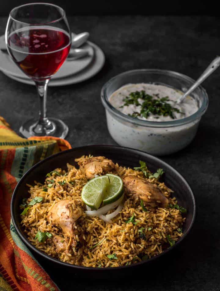 Chicken Biryani in a bowl with raita and wine
