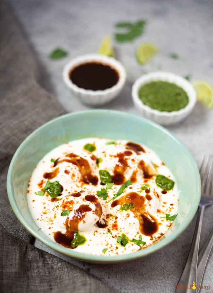 Lentil balls in thick yogurt topped with chutneys that are also in 2 small dipping bowls.