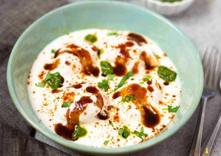 Dahi Vada in a green bowl topped with tamarind and green chutney