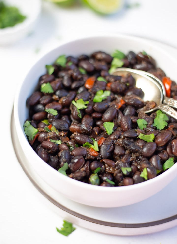 Chipotle Mexican Black beans in a white bowl garnished with cilantro and two silver spoon on side