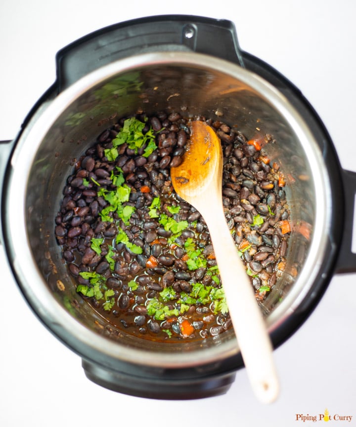 a wooden spoon stirring black beans with vegetables and cilantro inside an instant pot