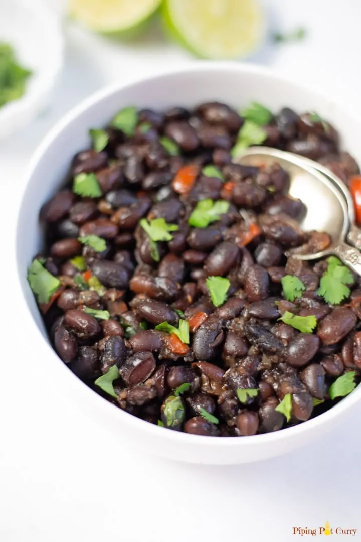 black beans with red peppers and cilantro in a white bowl with a silver spoon