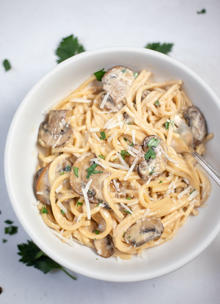 Creamy Spaghetti Pasta with mushrooms in a white bowl garnished with cheese and parsley