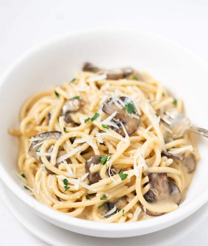 Pasta with mushrooms topped with parmesan and parsley in a white bowl