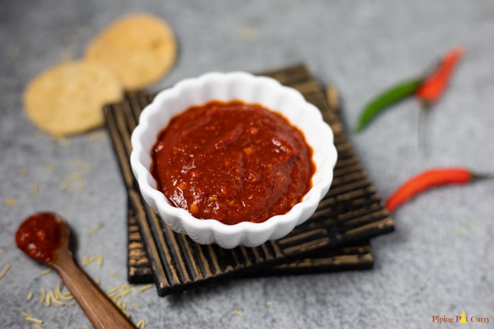 Red Chili Garlic Chutney in a small white bowl, with green and red chili and puri 