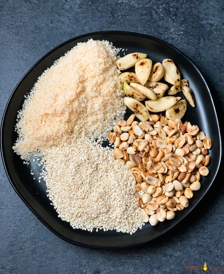 Ingredients such as roasted garlic, peanuts, sesame and coconut powder in a black plate