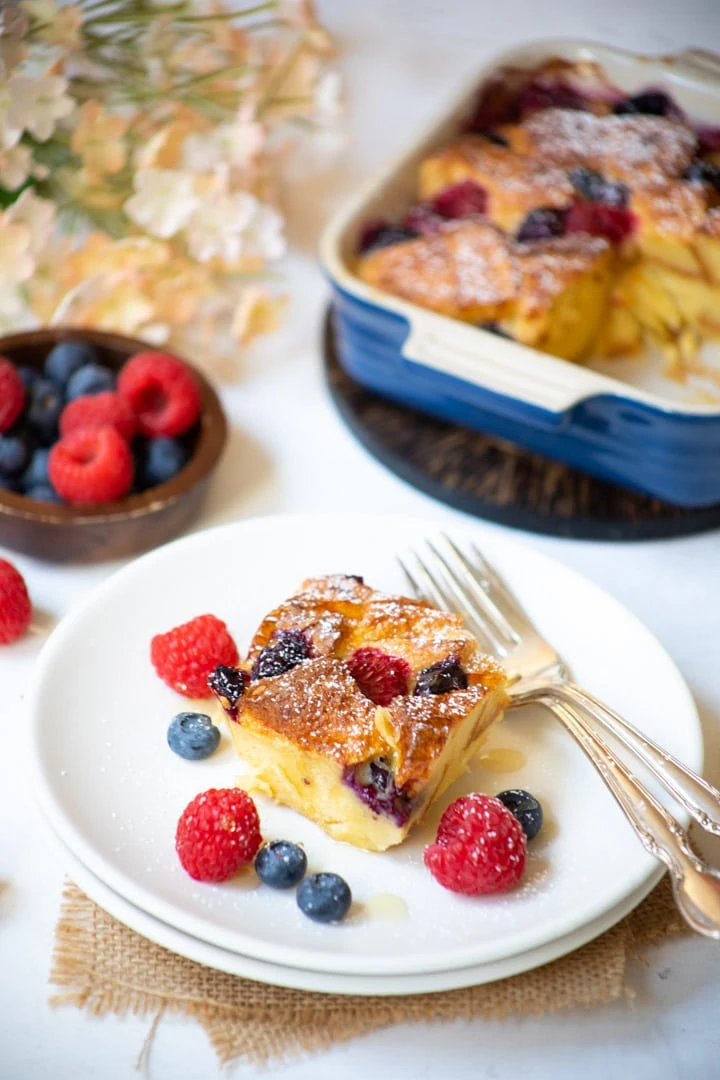 Berry Bread pudding served in a white plate with fresh berries on the side