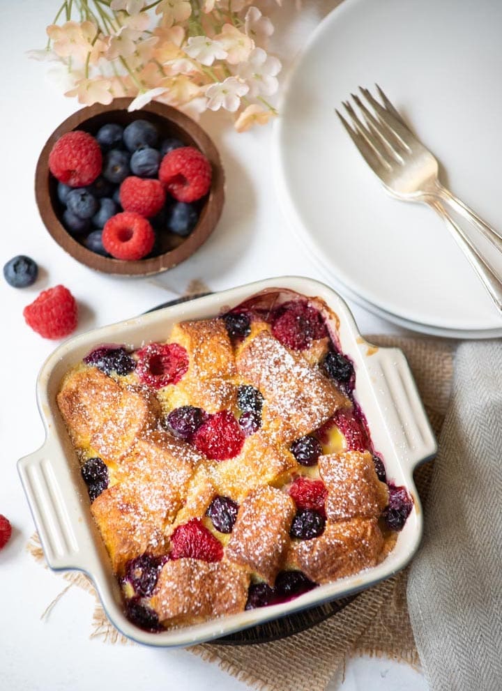 Berry bread pudding in a baking pan with berries on the side and some flowers