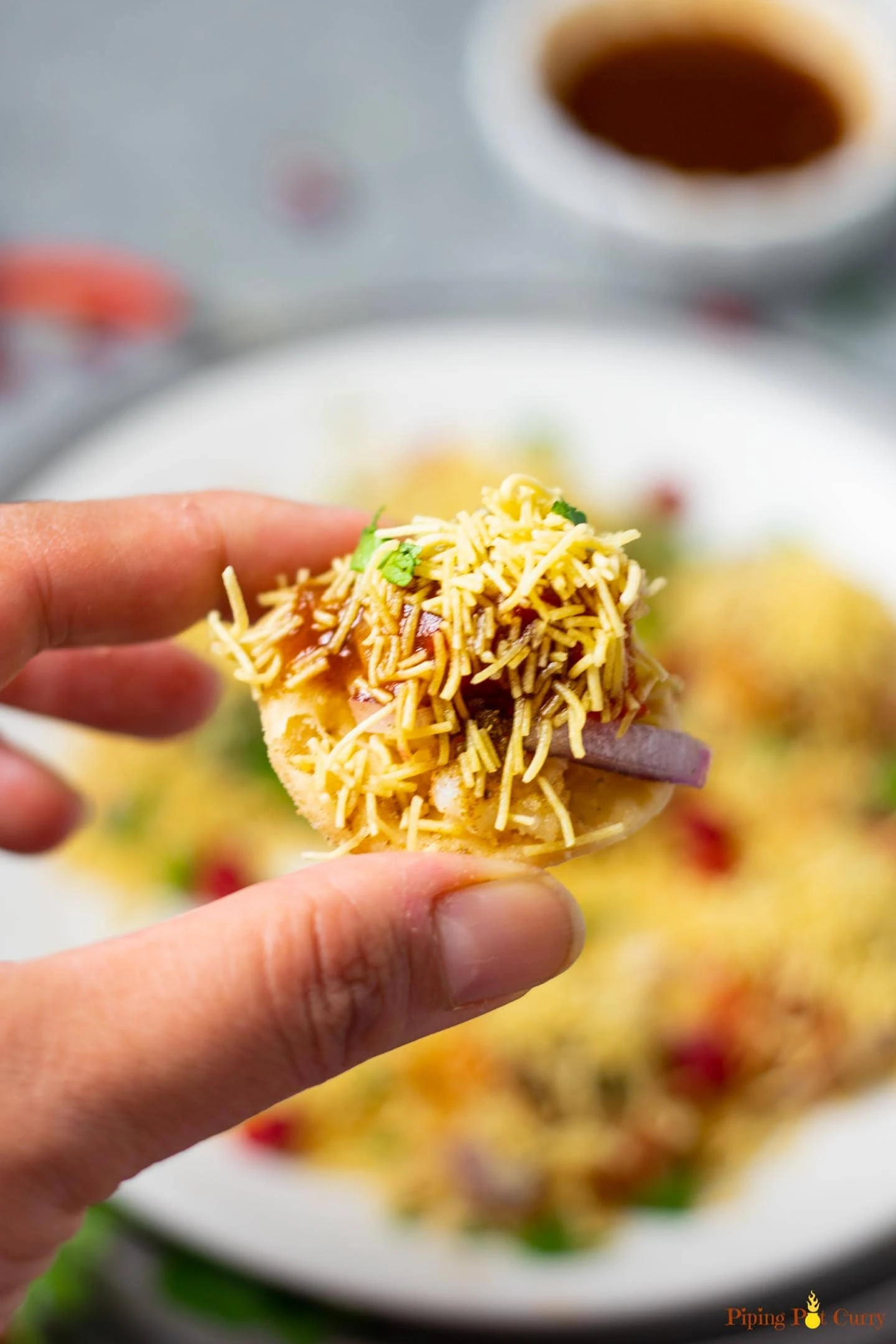 Closeup of a sev puri with a whole filled plate in the background