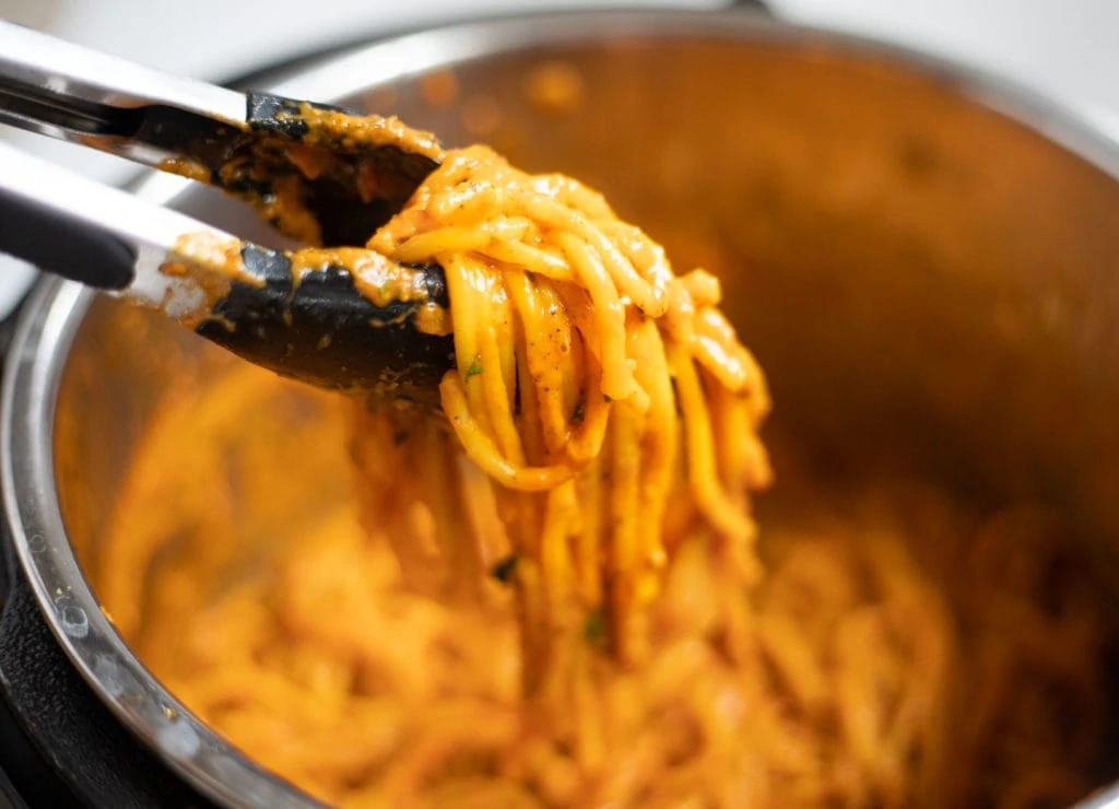Closeup of creamy tikka pasta in tongs over a pot