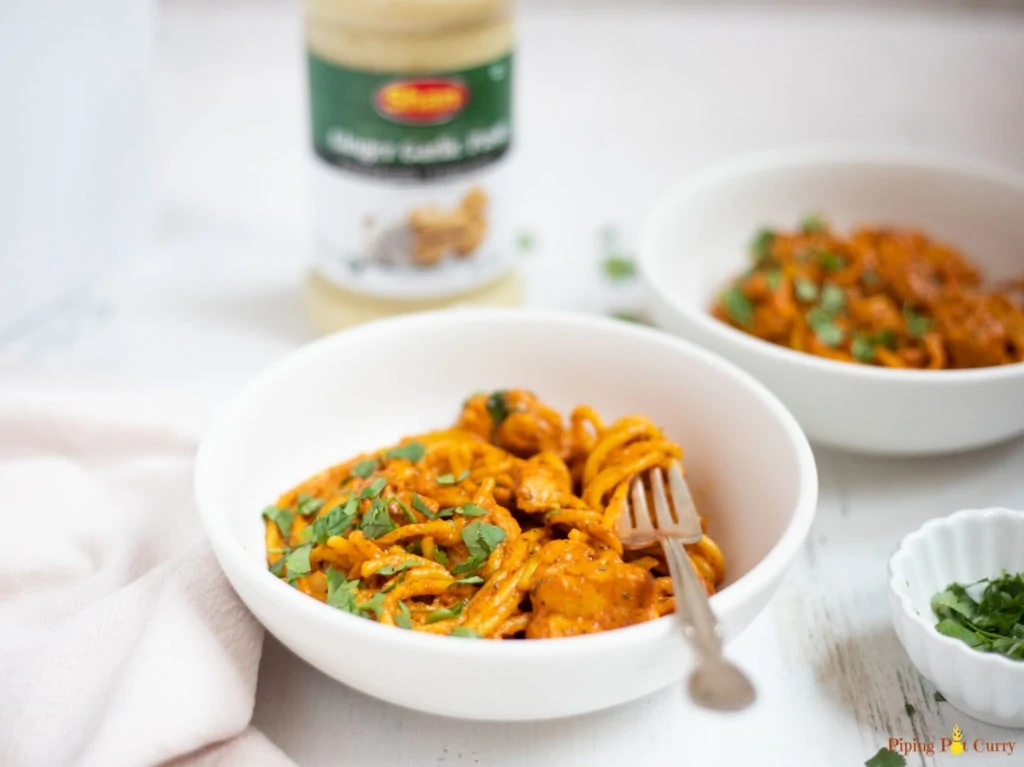 Creamy tikka masala pasta in 2 white bowls with cilantro and a bottle in the background