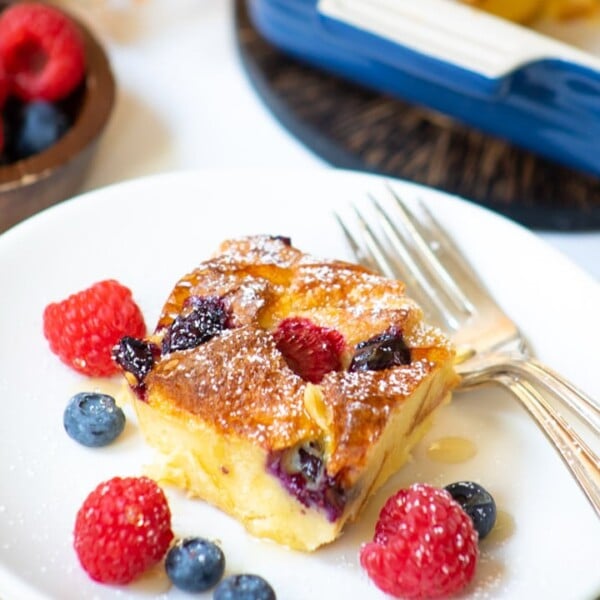 Berry Bread pudding served in a white plate with fresh berries on the side