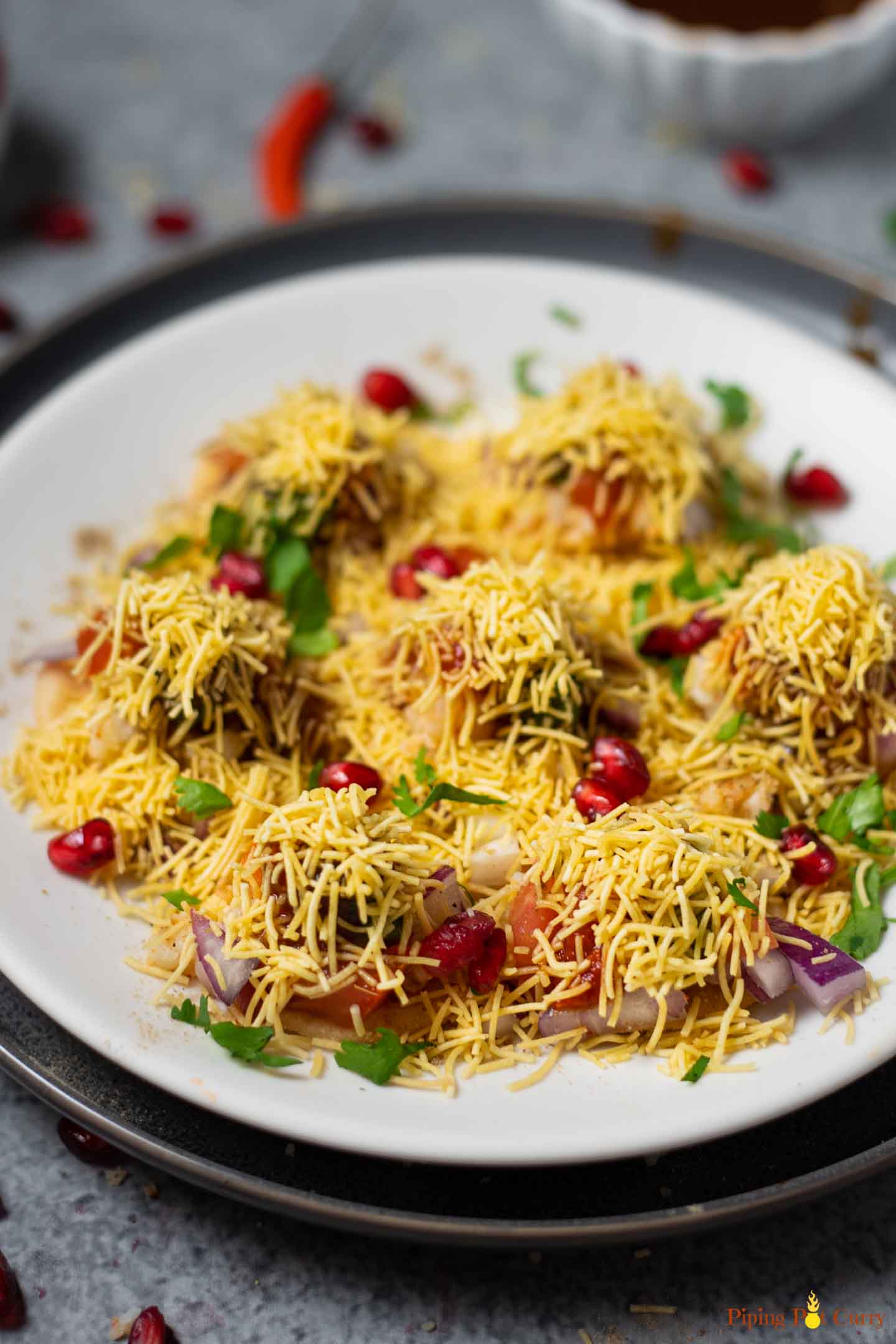 Sev puri garnished with cilantro and pomegranate seeds on a white plate