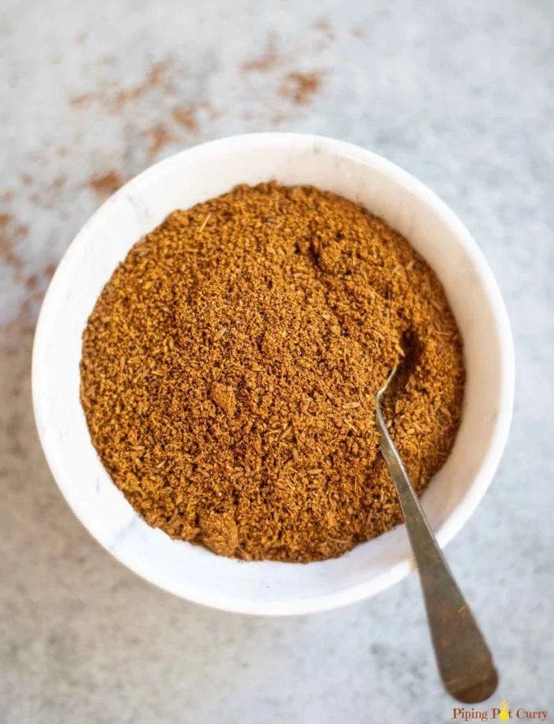 Cumin powder in a white bowl with a spoon