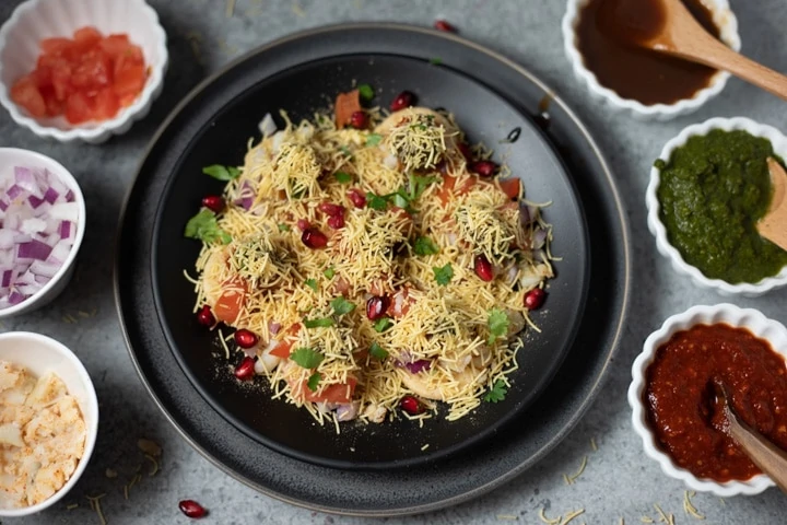 Sev puri garnished with pomegranate and cilantro in a black plate.
