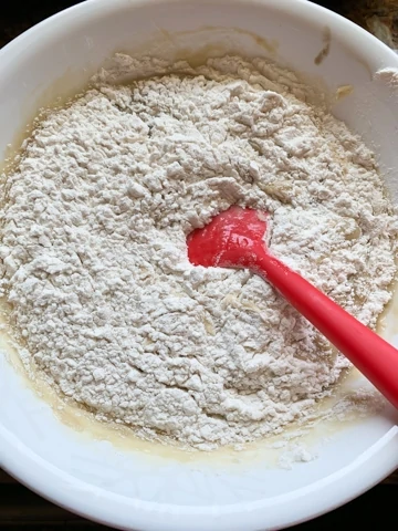flour on top of mashed bananas with a spatula in a white bowl