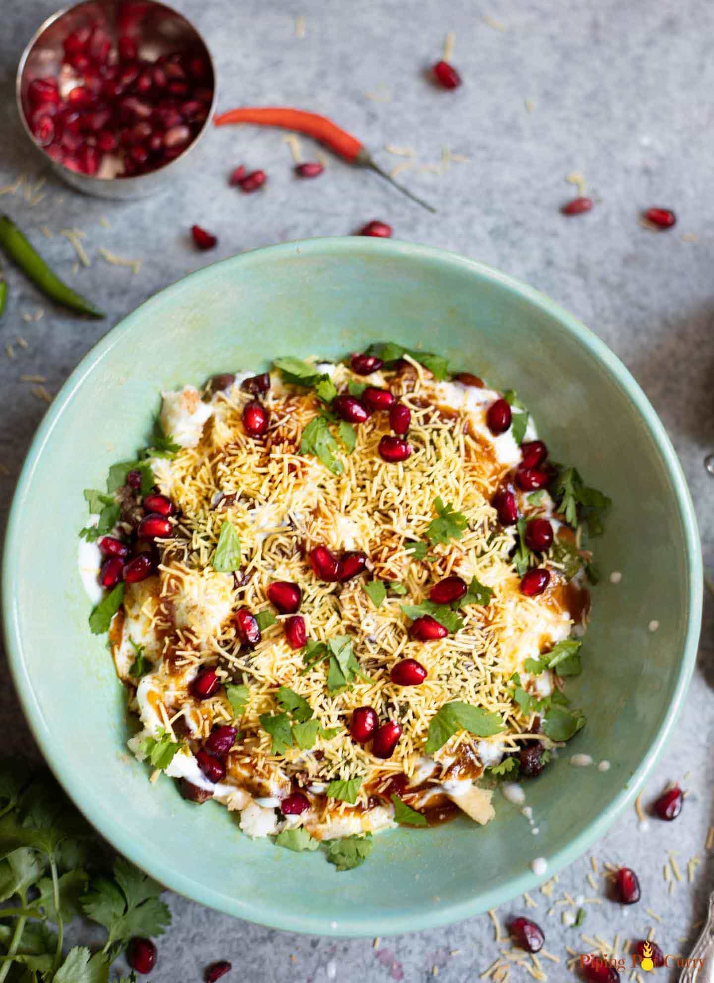 Dahi Papdi Chaat in a bowl with chutneys in the side and pomegranate seeds