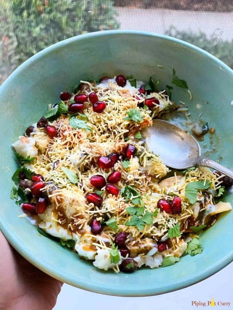 Hand holding papdi chaat street food in a green bowl 