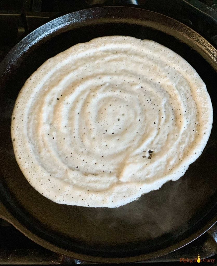 Dosa being made on a cast iron griddle 